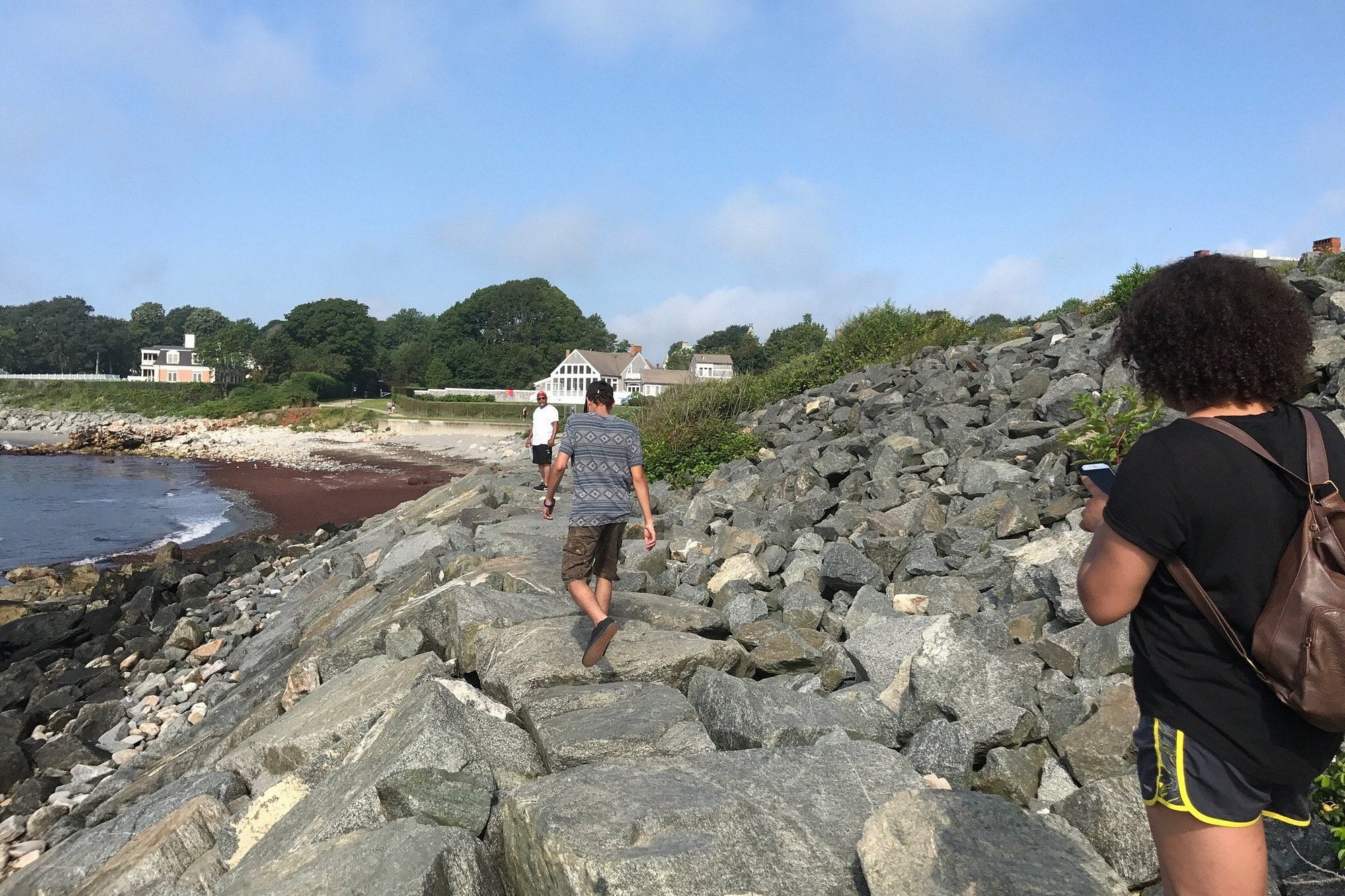 Hikers on the rocky shoreline path of the Cliff Walk